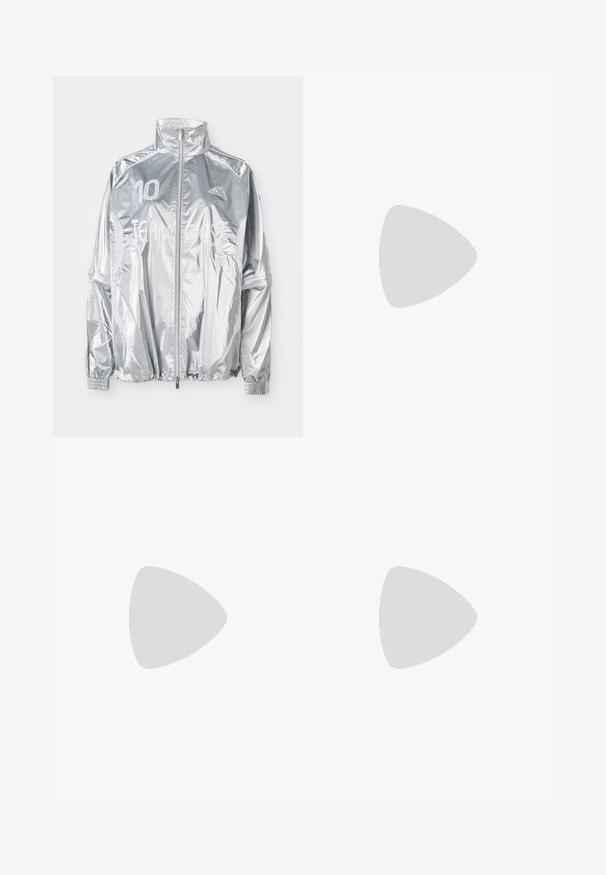 Hõbe värvi Adidas'i tõmblukujope kõrge kraega, elastsete mansettidega, vasakul rinnal number "10" ja ees tekst "TEAM GAST."; Valge nööpidega särk pika varrukaga, volangiga kõrge krae ja vertikaalne volangide aksent ees. Kerge puuvillane kangas.; Mustad laiad spordipüksid, mis on valmistatud pehmest kangast, elastse vöökohtaga ja väikese logoga vasakul küljel.; Mustad nahast spordijalatsid kolme valge triibuga ja mustade kingapaeltega. Kingade kõrval on osaliselt nähtavad tekstureeritud mustad püksid.