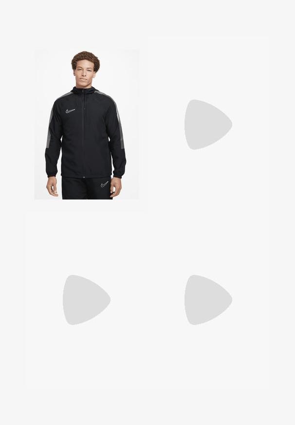 Nike Performance Vindjacka - black black white white; Vit fotbollströja med korta ärmar, gröna och röda detaljer på ärmsluten och kragen, mittens emblem samt vertikala färgstripes. Nike-logga närvarande.; Svarta träningsbyxor med elastisk midja, avsmalnande design, med en stor vit Nike-logotyp på vänster ben. Mjuk, lättviktig tyg.; Svarta träningsskor med en texturerad ovandel, vit Nike-logga och en vit gummisula. Har snörningsdesign och en dynamisk form.