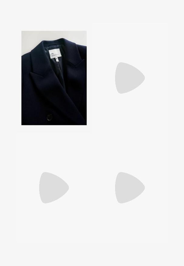 Mörk marinblå blazer i texturerat tyg med skarpa slag och dubbelknäppning. Invändigt har den en mjuk foder och varumärkesetikett.; Mörkblå långärmad topp med båtringning och rynkdetalj på sidan, liggande plant på en vit bakgrund.; Breda byxor i mörk marinblå färg, med en texturerad tyg, dragsko i midjan och en löst sittande silhuett för komfort.; Röda mockasko med vita ränder, snörningsdesign och en strukturerad brun gummisula. Bärs med svarta byxor, mot en blå matta.; Vitt fleecehalsduk med fransade kanter, mjuk textur och rektangulär form. Lämplig för lager-på-lager och för att ge värme.