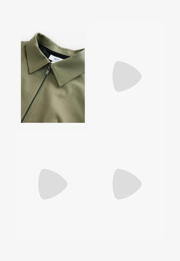 Olijfgroen jack met een visgraatstructuur, voorzien van een zwarte rits en een puntige kraag. Het label in de kraag zegt "NEXT".; Roze T-shirt met korte mouwen van katoen. Heeft een ronde halslijn en een losse pasvorm met een rechte zoom aan de onderkant.; Wijdvallende broek van donkergroene stof met witte verticale strepen, geplooide voorkant en een aansluitende tailleband met riemlussen.; Zwart-witte sneakers met een bovenwerk van suede en leer, voorzien van drie witte strepen, een geperforeerde neus en een rubberen gumzool.