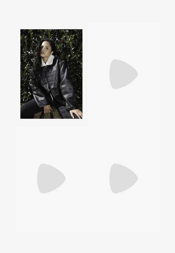 Svart konstläderjacka med vit fårskinnskrage, oversized passform, stora knappar och texturerad yta. Bärs med mörk denim, mot en grön bakgrund.; Brun bomull T-shirt med en avslappnad passform, rundat halsringning och korta ärmar. Har svart text "STIEGLITZ" på bröstet. Slät textur.; Blå denimjeans med bred bendesign, fem fickor, knappgylf och kontrasterande sömmar. Texturerad tyg med en blekt finish.; Mörkbruna läderstövlar med medellång design, gula sömmar, justerbara spännband och dragflikar upptill. Texturerad yta.