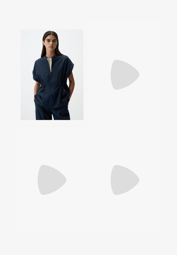 Veste courte bleu marine à manches courtes avec col montant, fermeture éclair sur le devant et taille ajustable par cordon, dotée de deux poches latérales et d'une texture de tissu lisse.; T-shirt blanc à manches courtes en coton léger. Présente un col rond et des manches retroussées. Étiquette logo rouge sur le col.; Shorts noirs en matériau doux, dotés d'une taille élastique avec cordon de serrage, de poches latérales et d'un design simple et épuré.; Baskets de course bleues avec des accents noirs, présentant une tige texturée, un col rembourré et une épaisse semelle intermédiaire noire et turquoise avec une semelle extérieure Vibram.; Lunettes de soleil blanches avec des verres marron, de forme ovale, fabriquées en plastique lisse, avec des accents gris sur les branches et un logo sur la monture.