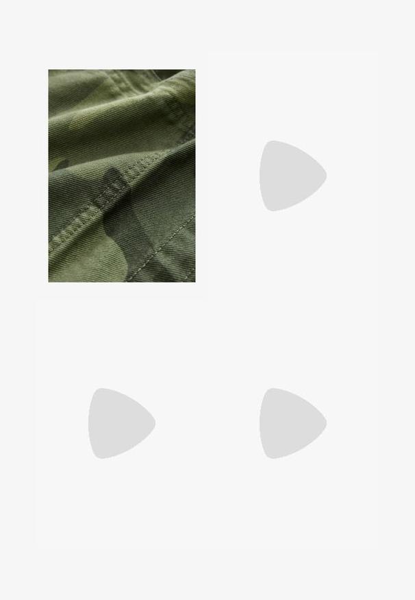 Grüner Camouflage-Stoff mit strukturierter Oberfläche, der subtile Musterabweichungen und sichtbare Nähte entlang der Kanten aufweist.; Raglan-T-Shirt in Creme mit dunkelblauen Ärmeln, auf der Vorderseite mit "ENGELNUMMERN 912-412" in Schwarz bedruckt. Mischgewebe aus Baumwolle.; Helleblaue Denim-Jeans im weiten Schnitt haben eine hohe Taille, fünf Taschen, dezente Ausbleichungen und Ziernähte entlang der Nähte.; Schwarze Wildledersneaker mit weißen Streifen und Akzenten, rundlicher Zehenbereich, Sohlen aus braunem Gummi, kombiniert mit weißen, gerippten Sneakersocken.