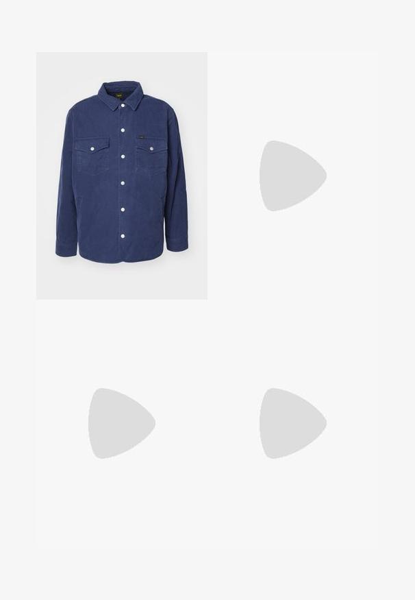 Veste chemisée matelassée marine avec deux poches poitrine, boutons-pression et col classique. Elle présente un motif texturé et une coupe décontractée.; Jeune homme aux cheveux châtains clair et bouclés, portant un t-shirt noir à manches courtes et un pantalon gris, regardant vers sa gauche les mains dans les poches.; Pantalons noirs en tissu lisse, avec une coupe droite, des plis avant et des passants de ceinture, offrant un design ajusté et structuré.; Mocassin en cuir noir avec un bout arrondi, des détails cousus et une sangle décorative à l'avant. Semelle plate avec un profil minimal.