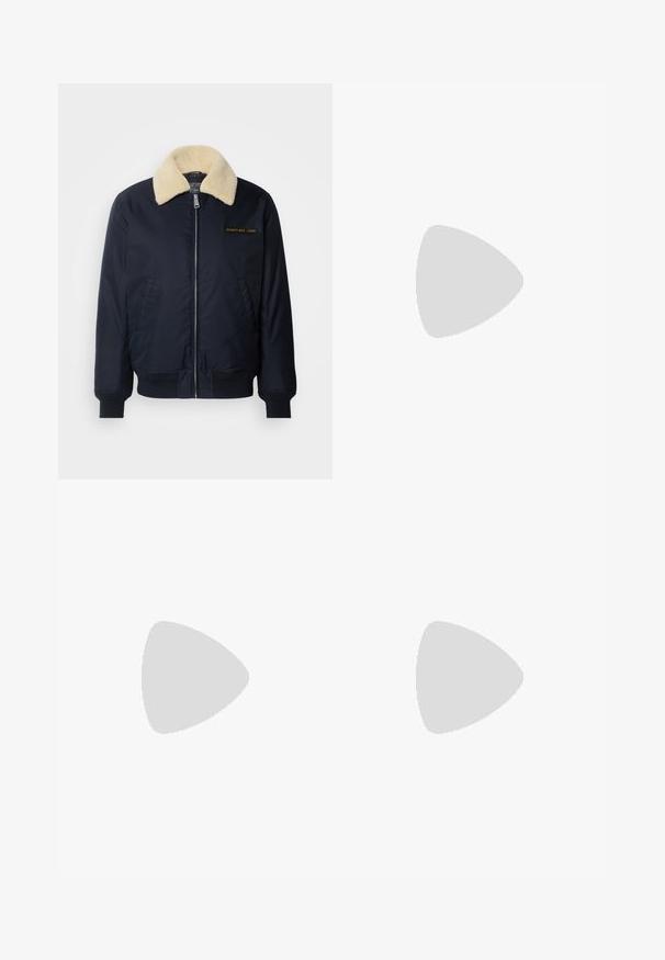 Marine bomberjakke med krèmefarget faux fur-krage, sidelommer, ribbestrikkede manchetter, glidelås foran og gull brodert logo på brystet.; Svart bomull T-skjorte med rund hals. Har en beige rektangulær grafikk og hvit tekst, "JAWO," sentrert på forsiden. Korte ermer.; Svart, elastisk midjebukser med rett ben-design, med en glatt tekstur og uten synlige mønstre eller maskinvare.; Hvite sneakers med glatt tekstur, med brune skinnakenter og svart detaljer, parret med svarte skreddersydde bukser. Bakgrunn med tregulv.