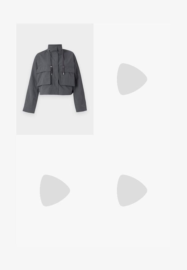 Jachetă gri, cropped, cu guler înalt, două buzunare mari în față, detalii cu șnur și un material ușor, texturat.; Tricou alb din bumbac cu o croială lejeră, mâneci scurte și un mic logo brodat în zona stângă a pieptului.; Pantaloni din denim albastru cu un design pe patchwork în nuanțe variate de albastru, cu talie cu șnur și picioare largi, cu croială dreaptă.; Tenisi albaștri din suede cu dungi albe, talpă din cauciuc, vârf rotund și șireturi din material. Asortați cu șosete crem pe o suprafață verde.