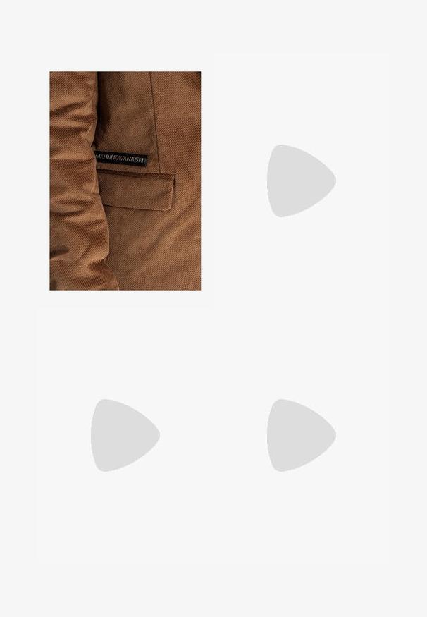 Ruskohvihta ruskea, jossa on vasemmalla puolella tasku ja etiketti, jossa on mustalla "Gráinne Kavanagh", näkyvät ompeluseikat kauttaaltaan.; Oliivinvihreä puuvillapaidan t-paita, jossa on suuri musta Levi's-logo edessä. Klassinen pyöreä kaula-aukko ja lyhyet hihat, sileä tekstuuri.; Vihreät kangashousut, jotka on valmistettu kestävästä puuvillasta. Ominaisuuksiin kuuluvat useat taskut, vetoketjulla varustettu sivutasku sekä kapenevat lahkeet, joissa on hieman teksturoitu pinta.; Mustat korkeat kangaslenkkarit, joissa on valkoiset kumipohjat ja nauhat, sivussa on pyöreä logo, ja ne on yhdistetty farkkuihin ja mustiin housuihin.