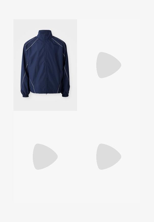 Jachetă de vânt de marine, material ușor, închidere cu fermoar pe față, guler înalt, manșete elastice și cusături de accent gri de-a lungul cusăturilor.; Tricou alb din bumbac cu mâneci scurte. Prezintă o grafică ovală centrală cu textul „New Era” în albastru închis. Croială simplă, clasică.; Pantaloni casual negri cu șnur la talie, cu buzunare laterale și croială dreaptă, pe un fundal simplu.; Pantofi sport negri, cu țesătură texturată și tălpi din cauciuc, având șireturi elastice și un accent albastru pe toc. Purtați cu pantaloni din denim deschis.