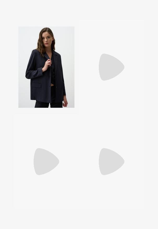Blazer navy a righe sottili in tessuto leggero, con colletto a punta, chiusura frontale con un bottone singolo e dettagli con tasche laterali.; Camicia di lino bianca a maniche lunghe, con colletto button-down e bottoni frontali. Presenta un piccolo logo ricamato blu sul petto.; Jeans in denim blu chiaro con taglio dritto, design a cinque tasche e chiusura con bottone. Presentano una leggera sbiaditura e dettagli in cucitura arancione.; Scarpa slip-on in suede marrone con tacco basso, cinturino regolabile con fibbia argentata e suola in gomma nera.
