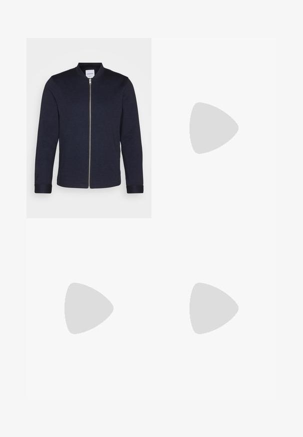 Casaco bomber azul-marinho escuro com fecho éclair frontal, gola redonda e mangas com punhos. Feito de um tecido suave com um design minimalista.; Camisa de manga longa azul e branca com riscas, feita de algodão, apresentando um colarinho abotoado, botões frontais e um pequeno logotipo bordado no peito.; Calças bege com uma textura suave, corte reto, dois bolsos traseiros com botões e uma cintura padrão.; Sneaker preto com sola branca flutuando acima de um tapete texturizado bege, perto de uma mesa redonda de madeira com livros empilhados.