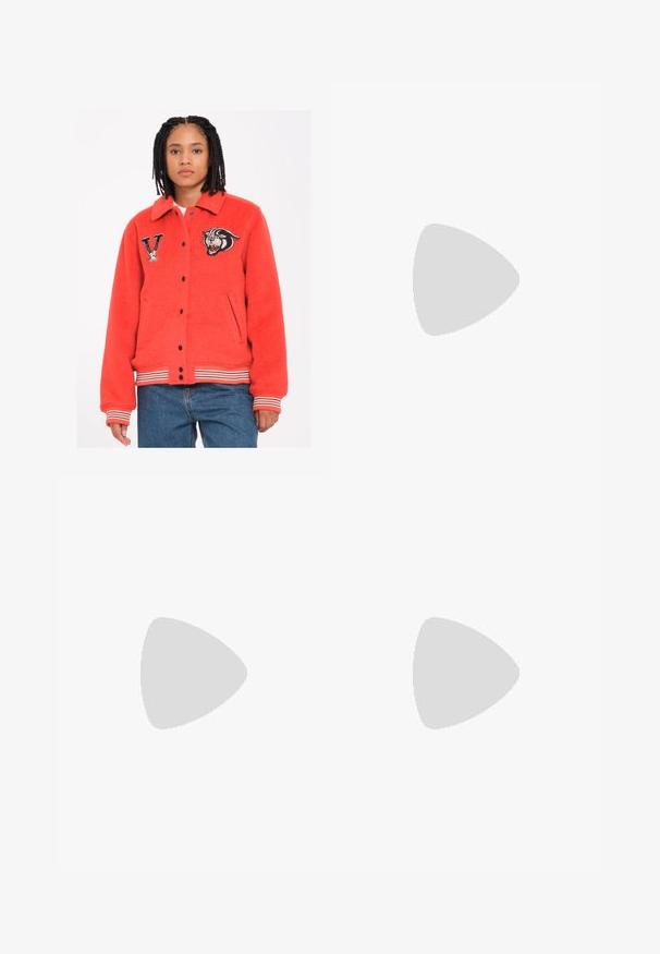 Rote Fleecejacke mit Kragen, schwarzen Druckknöpfen, Seitentaschen und gestreiften Bündchen. Mit gestickten Tiger- und Buchstaben-"V"-Aufnähern.; Weißes Baumwoll-T-Shirt mit einem schwarzen Rippenkragen, kurzen Ärmeln, schwarzen Streifen-Akzenten und einem gelben Smiley-Gesicht, das auf der Brust gestickt ist.; Cremfarbene, weit geschnittene Hosen mit einem Zickzackmuster, ausgestattet mit einem schwarzen Logo-Bund und seitlichen schwarzen Streifen. Leichter, strukturierter Stoff.; Blaue Wildledersneaker mit weißen Streifen, Gummisohle, runder Zehenform und textilen Schnürsenkeln. Kombiniert mit cremefarbenen Socken auf einer grünen Fläche.