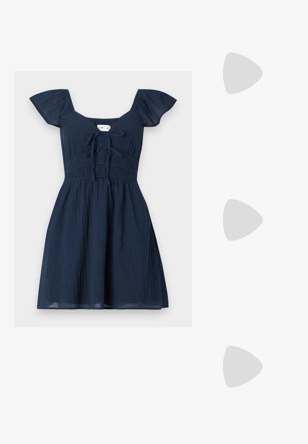 Hvid t-shirt med korte ærmer, rund hals og en lille blå trykt tekstdetalje på brystet. Lavet af blødt, letvægtsstof.; Marineblå kjole med flagrende ærmer, tekstureret stof og en tætsiddende liv, der har en frontbinding og en samlet talje.; Lyserøde ruskinds sneakers med grå detaljer, strømlinet design, tekstureret overdel og sort gummisål. Har Puma-logo på siden.; Sorte solbriller med wrap-around design, mørktonede linser, skinnende stjerneformede detaljer og justerbare næsepuder.