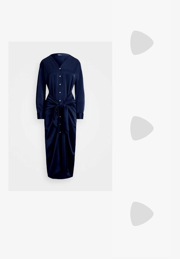 Granatowa sukienka z gładkiego materiału, z dekoltem w serek, zapinana na guziki, z długimi rękawami i wiązanym detalem w talii, posiadająca zwiewny dół.; Czarne skórzane sandały na obcasie z noskiem w szpic, z wycięciem z przodu i cienkim obcasem typu stiletto.; Złota kopertówka z cekinami o prostokątnym kształcie, z zakręconym uchwytem w postaci łańcuszka oraz metalowym zapięciem, odbijająca światło o fakturowanym wykończeniu.; Złote metalowe kolczyki w kształcie obręczy o zakrzywionym, wydłużonym kształcie. Posiadają gładką, błyszczącą powierzchnię oraz zaokrąglony koniec dla dodatkowego efektu.