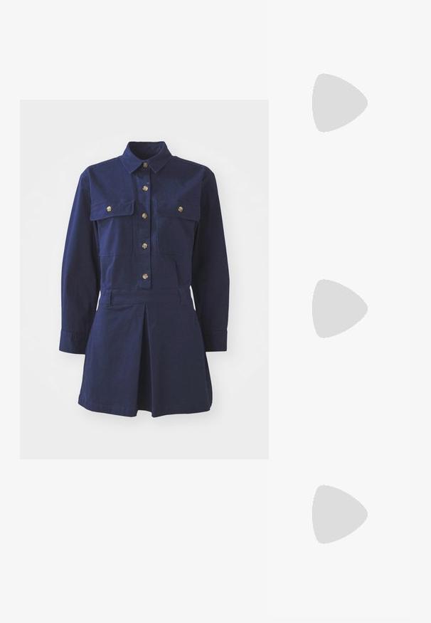 Robe chemise bleu marine en coton avec des manches longues, une fermeture à boutons à l'avant, deux poches poitrines et un détail de jupe plissée.; Sandale à talons hauts blanche avec une base de orteil plate, devant texturé avec des accents froncés et une fine bride à la cheville.; Pochette en métal argenté avec une forme douce et arrondie et un fermoir en haut noué. Fabriquée en simili cuir lisse.; Boucles d'oreilles en argent en forme de créoles avec un design torsadé, dotées d'une finition polie et d'une fermeture à poussoir. Mesurent environ 3 cm de diamètre.