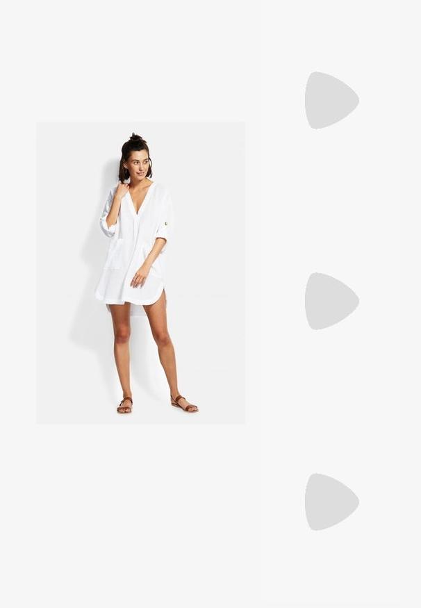 Weißes, leichtes Hemdkleid mit V-Ausschnitt, dreiviertelÄrmeln, Fronttaschen und lockerer Passform. Verfügt über minimale Nähdetails.; Weiße Slingback-Absätze mit spitzer Zehenpartie, glattem Obermaterial, niedrigem Blockabsatz und seitlichem Ausschnitt-Design mit verstellbarem Schnallenriemen.; Runde Sonnenbrillen mit dunklen Gläsern und goldenen Rahmen. Das Modell trägt eine hellblaue, gerippte Strickjacke mit Knöpfen und weißen Kontrastärmeln.; Michael Kors Clutch in beige beschichtetem Canvas mit einem wiederholten MK-Logo-Muster, goldfarbener hardware und einem abnehmbaren Kettenriemen.