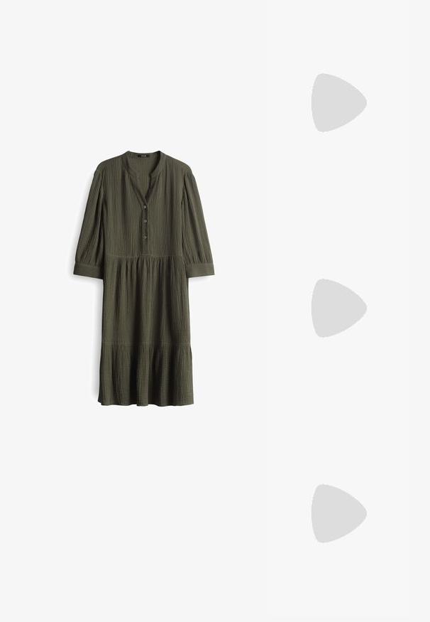 Olijfgroene jurk tot de knie van gekreukt stof. Heeft een henley-halslijn met drie knopen en geplooide mouwen. Uitlopende zoom.; Witte overhemdd, van katoen, lange mouwen, klassieke kraag, enkele borstzak, rechte zoom, minimale textuur, geen patronen.; Lage Nike sneaker in wit en donkergroen suede met bijpassende groene swoosh en een klein geel accent van een swoosh aan de zijkant.; ALDO PIGOWEN - Zonnebril - gold-coloured