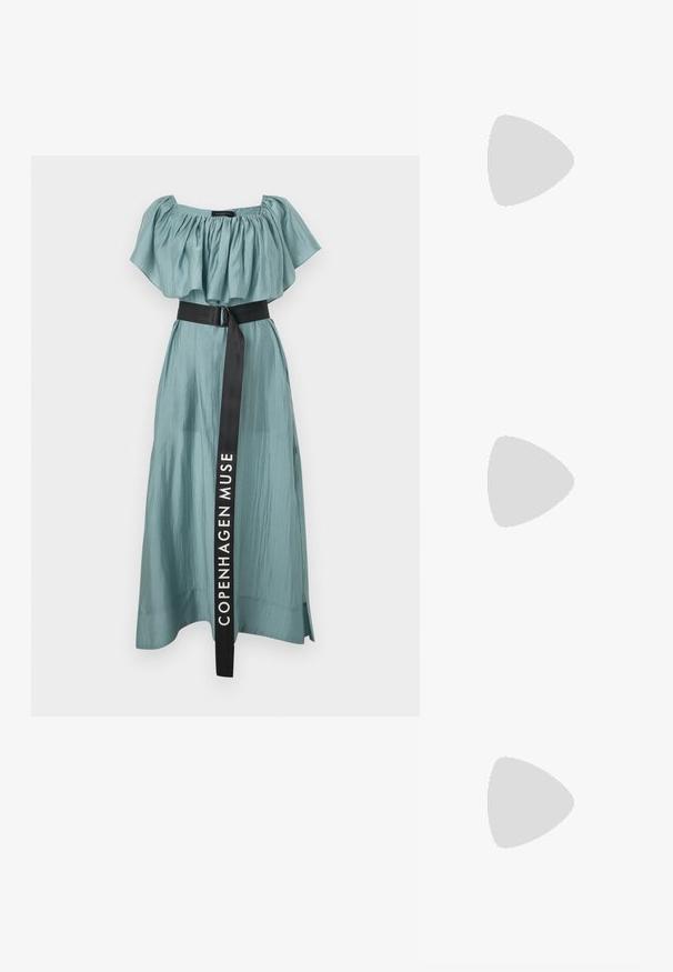 Pitkä, virtaava mekko haalean teal-värisestä kankaasta, jossa on kerätty olkapäiden yli kulkeva pääntie ja musta vyö, jossa on teksti "COPENHAGEN MUSE".; Musta lyhythihainen paita, joka on valmistettu sileästä materiaalista ja jossa on peplum-muotoilu sekä vyötäröllä vyö, jossa on kaksi pyöreää hopeanväristä nappia.; Mustat nahkakengät, joissa on terävä kärki ja matala lohkare korko. Varustettu nilkkahihnalla, jossa on kultasävyinen solki. Lisää sileä pinta.; Musta käsilaukku, jossa on rakenteellinen muoto, sileä pinta ja metallinen solki. Yhdistetty leveisiin mustiin housuihin ja avonaiheisiin sandaaleihin puulattialla.