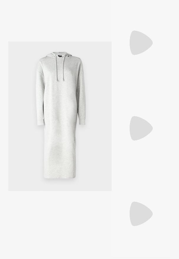 Dolga obleka s kapuco iz svetloživega blaga za trenirko, sproščenega kroja, z bočnimi odprtinami in vrvico na kapuci.; Črne usnjene gležnjarje z okroglo konico, vezalnim sprednjim delom in debelim gumijastim podplatom z teksturiranim profilom. Zanka na hrbtni strani.; Ženska z dolgimi temnimi lasmi, oblečena v črn kostim, nosi črno usnjeno torbo čez ramo in se ozira čez ramo proti beli podlagi.; Srebrne uhane v obliki obroča z minimalističnim dizajnom. Krožna oblika, gladka tekstura in tanek profil. Lahki s poliranim zaključkom.