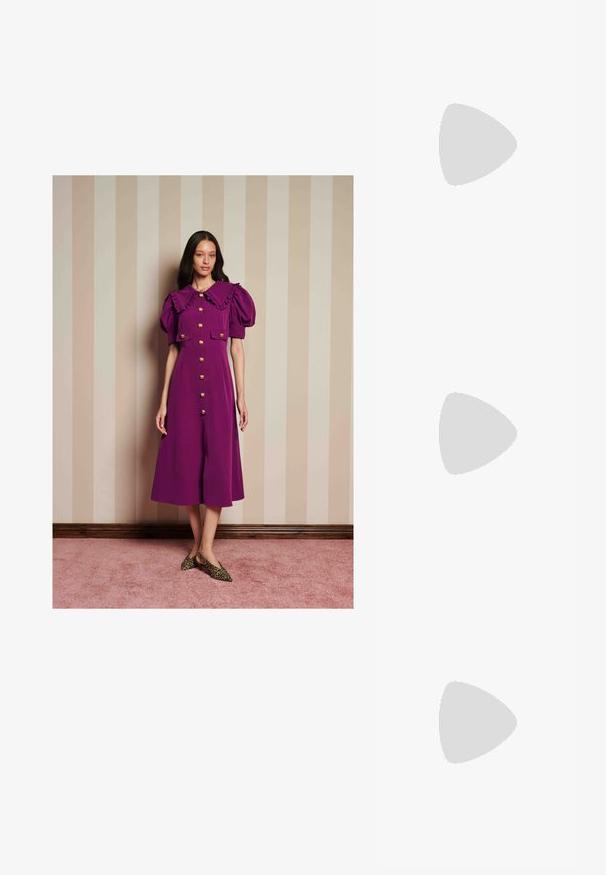 Kvinne står mot en stripete beige vegg iført en lilla kjole med puffermer, volangkrage, gullknapper og leopardmønstrede sko.; Høyhælte sandaler med et flerfarget, teksturert slangeprint. Har justerbare ankelremmer og en spiss tådesign.; Gull clutch-veske med en jevn metallisk finish, rektangulær form og en enkel lås. Ingen synlige mønstre eller dekorasjoner.; Gullde hoop øredobber med en bølgete, teksturert design. Har en tynn trådåpning og en polert, reflekterende overflate.