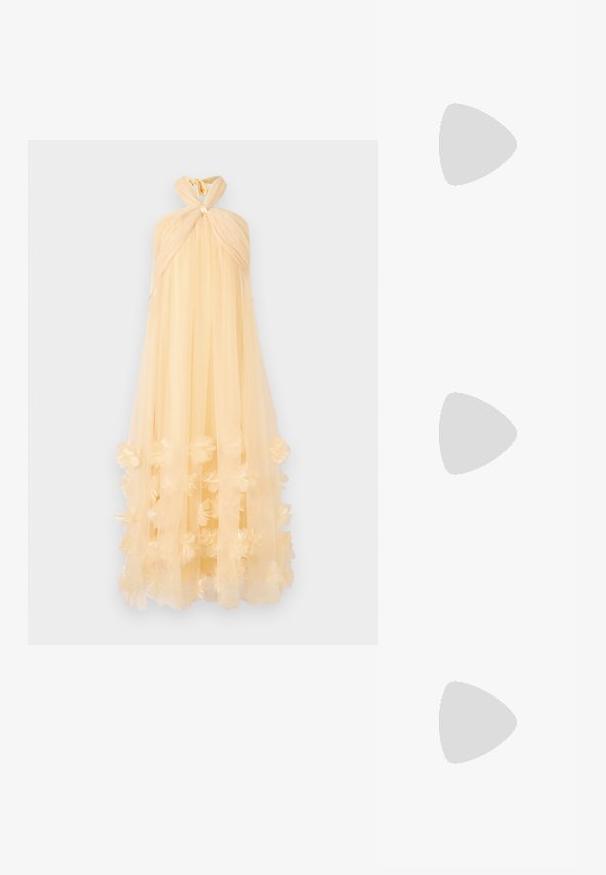 Maxi-jurk van doorschijnende, lichtgele stof, met een geknoopte halternek en bloemapplicaties aan de onderrand, wat een vloeiende silhouette creëert.; Witte leren sneakers, laag model, met een gladde textuur, ronde neus, vetersluiting aan de voorkant en een klein geborduurd logo aan de zijkant.; Zwarte leren halfronde tas met een gouden hardware accent, voorzien van een ritssluiting. Draagt crossbody over een grijze trui.; Gouden knoopstuds met een gedraaide design. Elke oorring heeft een ronde transparante achterkant voor een veilige draagervaring.