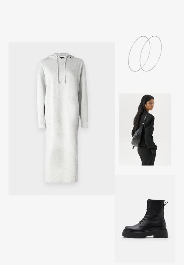 Dolga obleka s kapuco iz svetloživega blaga za trenirko, sproščenega kroja, z bočnimi odprtinami in vrvico na kapuci.; Črne usnjene gležnjarje z okroglo konico, vezalnim sprednjim delom in debelim gumijastim podplatom z teksturiranim profilom. Zanka na hrbtni strani.; Ženska z dolgimi temnimi lasmi, oblečena v črn kostim, nosi črno usnjeno torbo čez ramo in se ozira čez ramo proti beli podlagi.; Srebrne uhane v obliki obroča z minimalističnim dizajnom. Krožna oblika, gladka tekstura in tanek profil. Lahki s poliranim zaključkom.