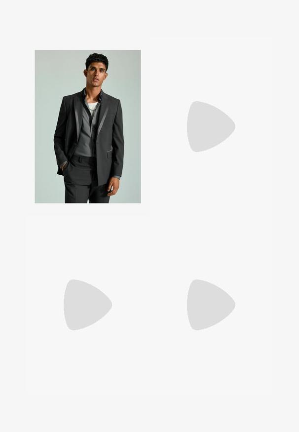 Abito grigio scuro con dettagli in satin, blazer abbottonato e pantaloni su misura. Sotto indossa una camicia grigio chiaro sovrapposta a una maglietta bianca.; Giovane uomo con capelli ricci di castano chiaro che indossa una t-shirt nera a maniche corte e pantaloni grigi, che guarda verso sinistra con le mani nelle tasche.; Pantaloni in corduroy neri con un design a gamba dritta, caratterizzati da sottili righe verticali e una vita standard. Nessun abbellimento visibile.; Sneakers in pelle blu navy con finitura liscia, suola piatta in gomma bianca, punta rotonda e sei lacci blu navy infilati attraverso occhielli rotondi.