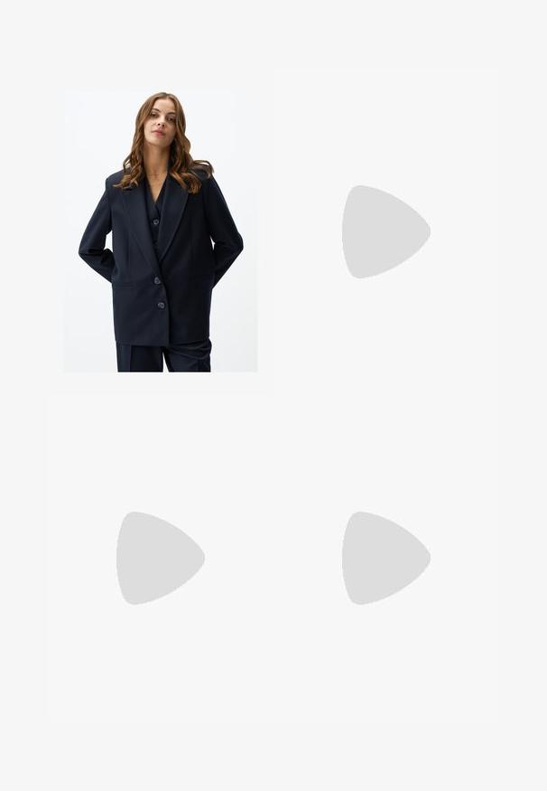 Blazer navy con design doppiopetto, rever a punta e due tasche frontali. Realizzato in tessuto liscio, presenta tre bottoni grandi.; Camicia a righe gialle con maniche lunghe, colletto a punta e chiusura frontale con bottoni. Presenta righe verticali blu e una vestibilità sartoriale.; Jeans larghi marroni in denim, caratterizzati da una chiusura frontale con bottone, cinque tasche e dettagli di cucitura visibili.; Mule gialli in ecopelle con punta affusolata, tacco aperto e un piccolo tacco a blocco. Presentano un nastro decorativo sul davanti.