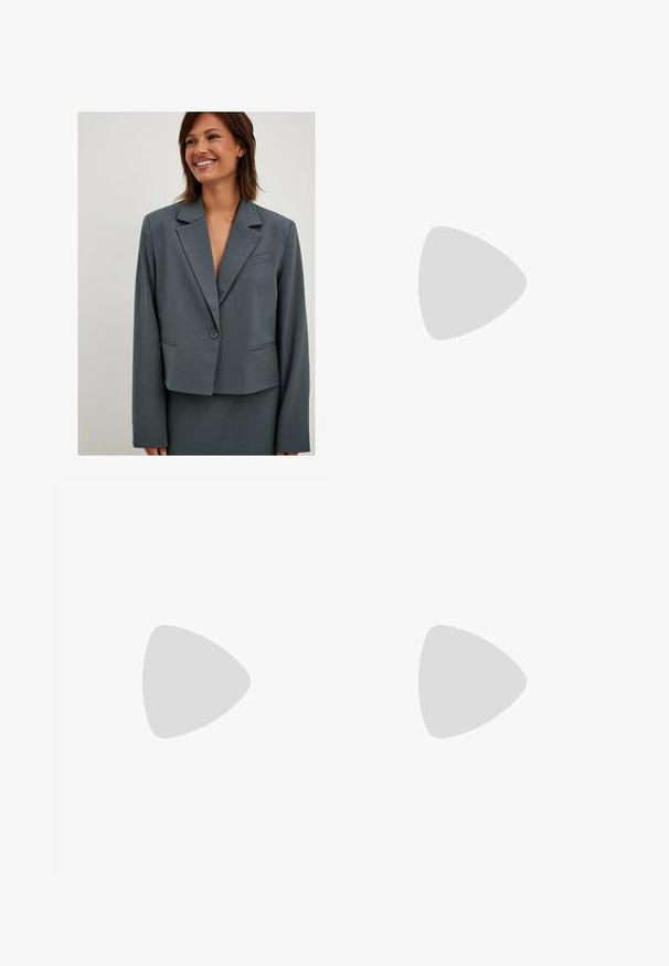 Blazer grigio su misura con chiusura a un bottone, rever a punta e due tasche frontali; realizzato in tessuto liscio e strutturato.; Due top in maglia senza maniche, a collo alto, in nero e bianco, con un design aderente e una superficie liscia, di lunghezza cropped.; Pantaloni neri a gamba larga realizzati in tessuto leggero, caratterizzati da una chiusura frontale con bottone e frontale piatto, con orli cuciti con precisione.; Scarpe sportive con tomaia in pelle bianca, punta in suede grigia e tre strisce nere. Presentano un logo blu sulla linguetta e una suola in gomma testurizzata.