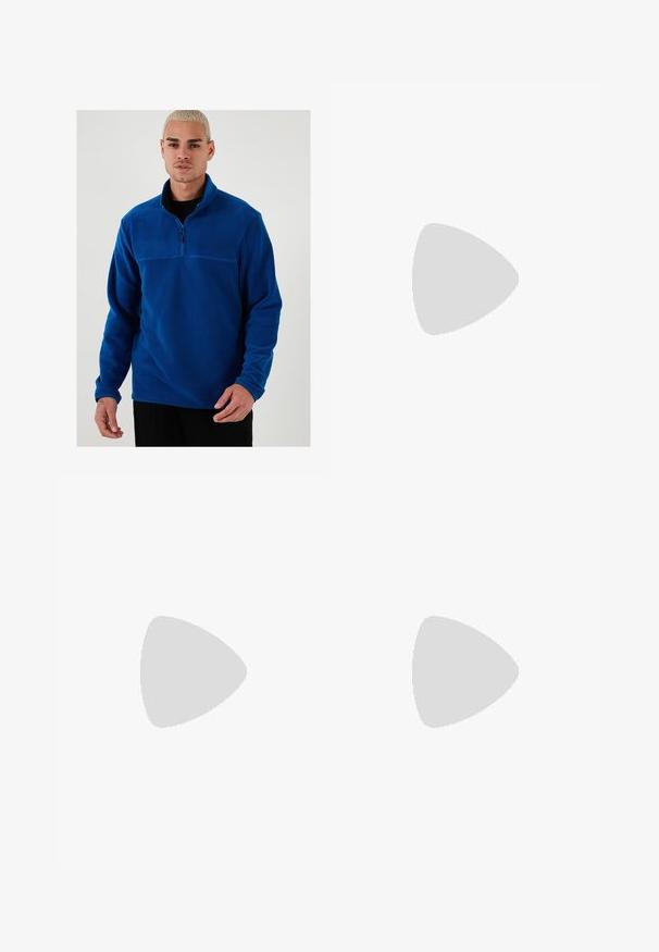 Blauer Fleece-Pullover mit einem Viertel-Reißverschluss auf der Vorderseite, langen Ärmeln und glatter Textur. Verfügt über ein kontrastierendes Panel über der Brust.; Drei weiße, gerippte Tanktops aus Baumwolle. Merkmale einen Rundhalsausschnitt und kleine schwarze Etiketten am Saum. In mehreren Größen erhältlich.; Weite blaue Denim-Jeans mit einer ausgewaschenen Optik, Fünf-Taschen-Design und einer Knopfverschluss. Ausgestattet mit Gürtelschlaufen und gestickten Details.; Braune Leder-Mokassins mit Quastenakzenten, strukturierten Oberflächen und kontrastierenden gelben Nähten entlang der schwarzen Gummisohle. Seitenansicht.