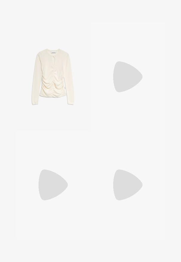 Langsleeve, ronde hals top in crème met gevouwen zijdetails en een sleutelgatopening bij de halslijn. Zacht, rekbaar materiaal.; Lichtblauwe denim jeans met een slanke pasvorm, hoge taille, vijf-pocket ontwerp, lussen voor een riem en een knoopsluiting.; Beige sneakers met donkergroene strepen, rubberen zool, bovenwerk van suede en textiel, en neutrale hardware, gecombineerd met bruine sokken op een lichtblauwe ondergrond.; Gouden metalen oorbellen in de vorm van een gebogen, verlengde hoop. Kenmerkend zijn het gladde, glanzende oppervlak en de afgeronde punt voor extra detail.