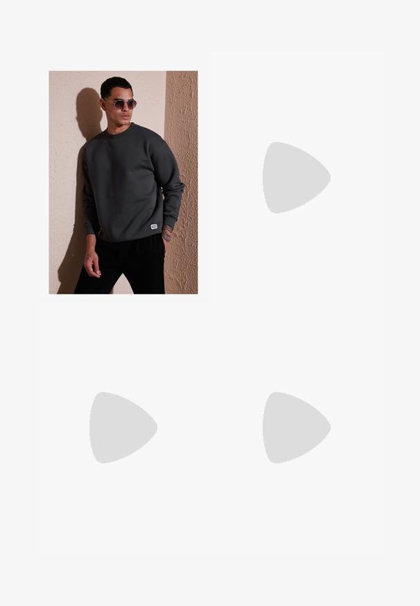 Sweatshirt grigio scuro con scollo a girocollo, polsini a costine e una piccola etichetta con il logo sulla sottoveste, abbinato a occhiali da sole tondi.; Jeans in denim blu a gamba larga con lavaggio sbiadito, design a cinque tasche e chiusura con bottone. Dotati di passanti per cintura e dettagli cuciti.; Sandalo marrone a due cinturini con fibbie in tono rame, plantare in sughero e suola in gomma. Design elegante con cinturini regolabili per una vestibilità ottimale.; Pendente d'argento con un design a onda intrecciato con il volto di un leone, appeso a una catena spessa. La superficie texturizzata aggiunge dettagli.