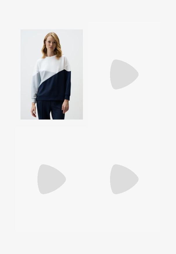 Colorblock sweatshirt in wit, lichtblauw en marineblauw; heeft een ronde halslijn en lange mouwen met ribgebreide manchetten. Zachte stoftextuur.; Zwarte katoenmix broek met een rechte pijpdesign, sluiting met een knop aan de voorkant en twee zijzakken. Soepele textuur, geen zichtbare patronen.; Bruine lakleren loafer met vierkante neus, metallic kettingaccent en lage blokhak; gladde textuur, minimalistisch ontwerp.; Zwarte handtas met gestructureerde vorm, gladde textuur en een metalen sluiting. Gecombineerd met brede zwarte broeken en sandalen met open teen op een houten vloer.