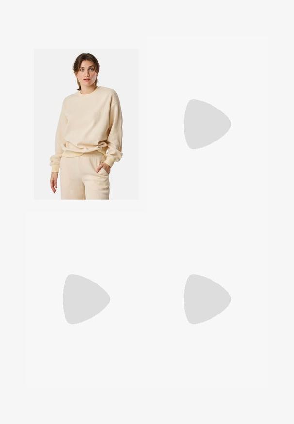 Beige geribde sweatshirt met lange mouwen, ronde hals en een relaxed fit. Het materiaal lijkt zacht en textuur te hebben, wat visuele interesse creëert.; Zwarte wijde sweatpants met een elastische tailleband, met witte zijstrepen en een geborduurd logo op de linker dij.; Zwarte suède sneakers met witte strepen en accenten, ronde neus, gum rubberen buitenzool, gecombineerd met witte geribbelde crewkousen.; Zwarte leren handtas met twee korte handvatten, zilverkleurige hardware, witte accenten en een wit logo. Heeft een gestructureerd oppervlak en een compact ontwerp.