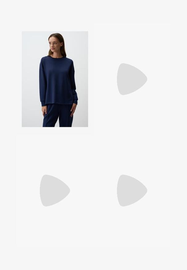 Felpa blu navy in morbido materiale, con maniche lunghe, collo rotondo e vestibilità comoda. Abbinata a pantaloni coordinati.; Shorts in denim di blu medio, con design classico a cinque tasche, chiusura con bottone e gamba dritta. Texture leggermente sbiadita in tutto il capo.; Scarpe sportive con tomaia in pelle bianca, punta in suede grigia e tre strisce nere. Presentano un logo blu sulla linguetta e una suola in gomma testurizzata.; Occhiali da sole neri oversize con lenti ovali, montatura in plastica liscia e accenti dorati sulle tempie. Le lenti scure offrono protezione dal sole.; Cesto di paglia intrecciata con una forma svasata, caratterizzato da una base e manici in pelle nera. Fibra naturale testurizzata con dettagli neri lisci.; Orologio rettangolare dorato con quadrante bianco, indicatori delle ore minimalisti e cinturino in metallo a rete. Presenta una corona laterale per la regolazione dell'ora.