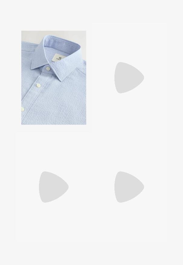 Lichtblauw gestructureerd shirt met een button-down kraag, voorzien van twee witte knopen en een label met de merknaam aan de binnenkant van de kraag.; Zwarte rechte spijkerbroek met vijf zakken en knoopsluiting, met een klein wit logo op de zijkant van de voorkant zak.; Zwarte leren instapper met kwastjes, gele stiksels langs de zool en een dikke, gegroefde rubberen buitenzool.; Zwarte rechthoekige zonnebril met donkere lenzen. Kunststof frame met een glanzende afwerking, met een brede neusbrug en licht taps toelopende pootjes.