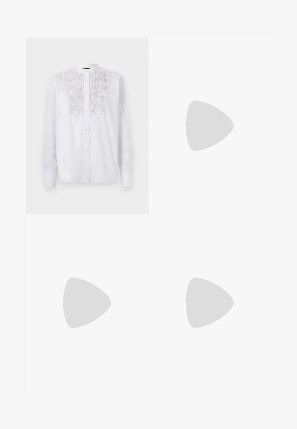 Chemise blanche à boutons avec un détail floral texturé sur la poitrine, des manches longues et un col Mao. Tissu en coton lisse.; Pantalons larges noirs en tissu texturé, avec une taille élastique et une ceinture à nouer amovible à la taille pour un ajustement variable.; Sandale à talon ouvert noire avec des brides croisées, une sangle de cheville ajustable et un talon épais, dotée d'une texture en cuir lisse.; Sac à main noir à la forme structurée, texture lisse et fermoir métallique. Associé à un pantalon noir ample et des sandales ouvertes sur un sol en bois.