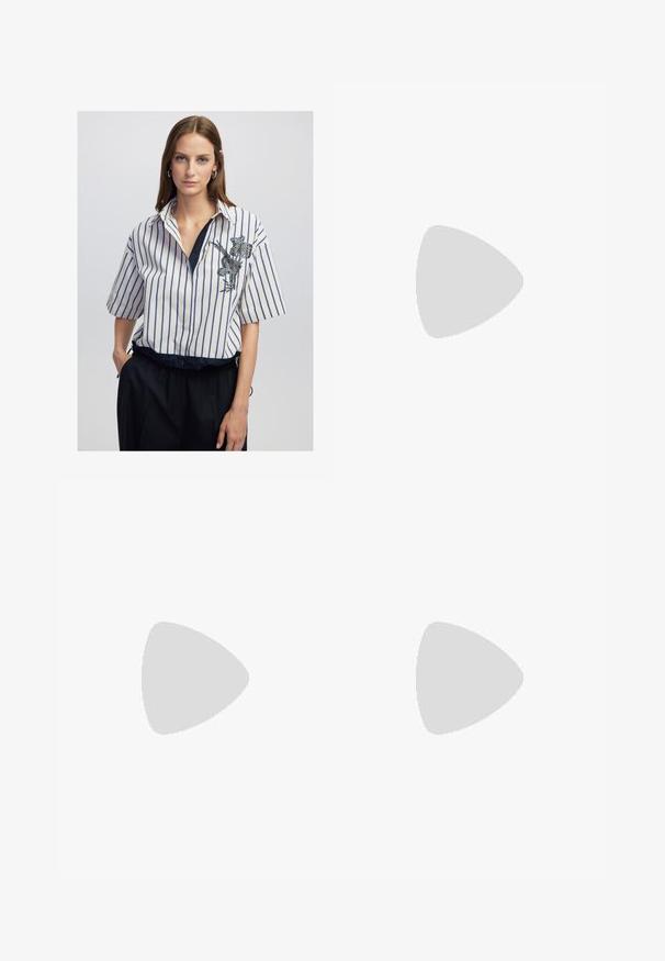 Una donna con capelli castani lisci indossa una camicia a righe verticali bianche e blu con ricami floreali, infilata in pantaloni neri, in piedi con una mano in tasca.; Pantaloni a gamba larga bianchi realizzati in un tessuto leggero. Presentano una vita elastica con cordoncino e tasche laterali. Texture liscia.; Sandali con tacco in vernice nera, con punta squadrata, cinturini alla caviglia e fibbie in argento. Presentano un tacco a blocco spesso per maggiore stabilità.; Occhiali da sole color crema con lenti ovali, tonalità nera e accenti metallici con logo alle tempie. Texture liscia, design a occhio di gatto.; Borsa a tracolla nera in pelle con una forma curva, manico rimovibile e accessori dorati. La borsa presenta una patta con un dettaglio a fibbia.