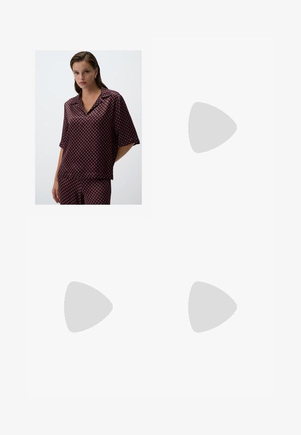 Rode en marineblauw geometrisch patroon blouse van lichtgewicht stof, met een kraag en korte mouwen, in een ontspannen pasvorm.; Zwarte wijde broek met hoge taille, knoopdetails op de tailleband en plooien aan de voorkant.; Zwarte leren pump met een spitse neus en een lage blokhak. Beschikt over een enkelband met een goudkleurige gespsluiting. Gladde textuur.; Zwarte handtas met gestructureerde vorm, gladde textuur en een metalen sluiting. Gecombineerd met brede zwarte broeken en sandalen met open teen op een houten vloer.