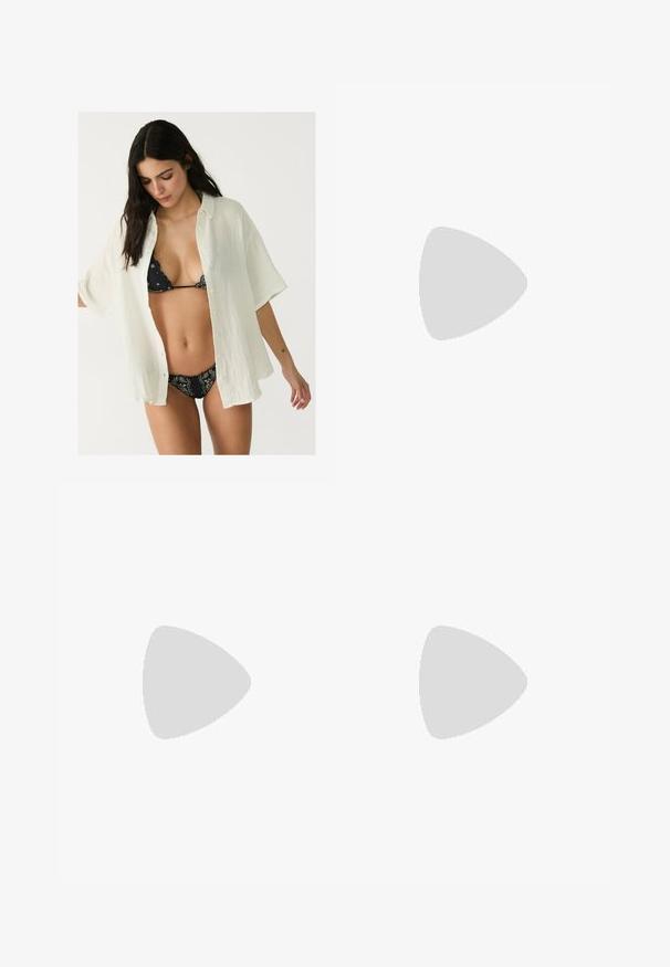 Weißes, übergroßes Button-up-Hemd aus strukturiertem Stoff, offen über einem schwarzen gemusterten Bikini getragen. Kurze Ärmel und eine lockere Passform.; Weiße weit geschnittene Hose aus leichtem Stoff. Mit einem elastischen Bund und Kordelzug sowie Seitentaschen. Glatte Textur.; Schwarze flache Sandalen mit einem Riemen-Design, das mehrere Lederstraps und eine schmale Schnalle am Knöchel umfasst. Die Sohle ist flach und rechteckig.; Weiße Schultertasche mit texturierter Oberfläche, zentralem Schnallenakzent und geschwungener Form. Reißverschluss an beiden Seiten.