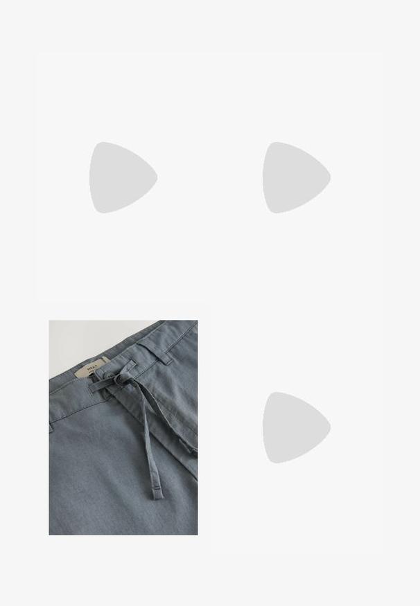 Lange mouw crèmekleurige geribbelde henley-shirt met een ronde halslijn, drieknoopssluiting en strakke manchetten, gecombineerd met donkere spijkerbroeken.; Grijze stoffen shorts met een zachte textuur, voorzien van een geknoopte trekkoord en riemlussen. Label geeft aan "NEXT" merk bij de tailleband.; Bruine suède slipper sandalen met twee verstelbare zilveren gespen, zwarte gestructureerde zool en geperforeerde details op het bovenste gedeelte.;  Schildpadzonnebril met groene lenzen, ronde vorm, gouden accenten en donkergroene pootjes met een witte streep.